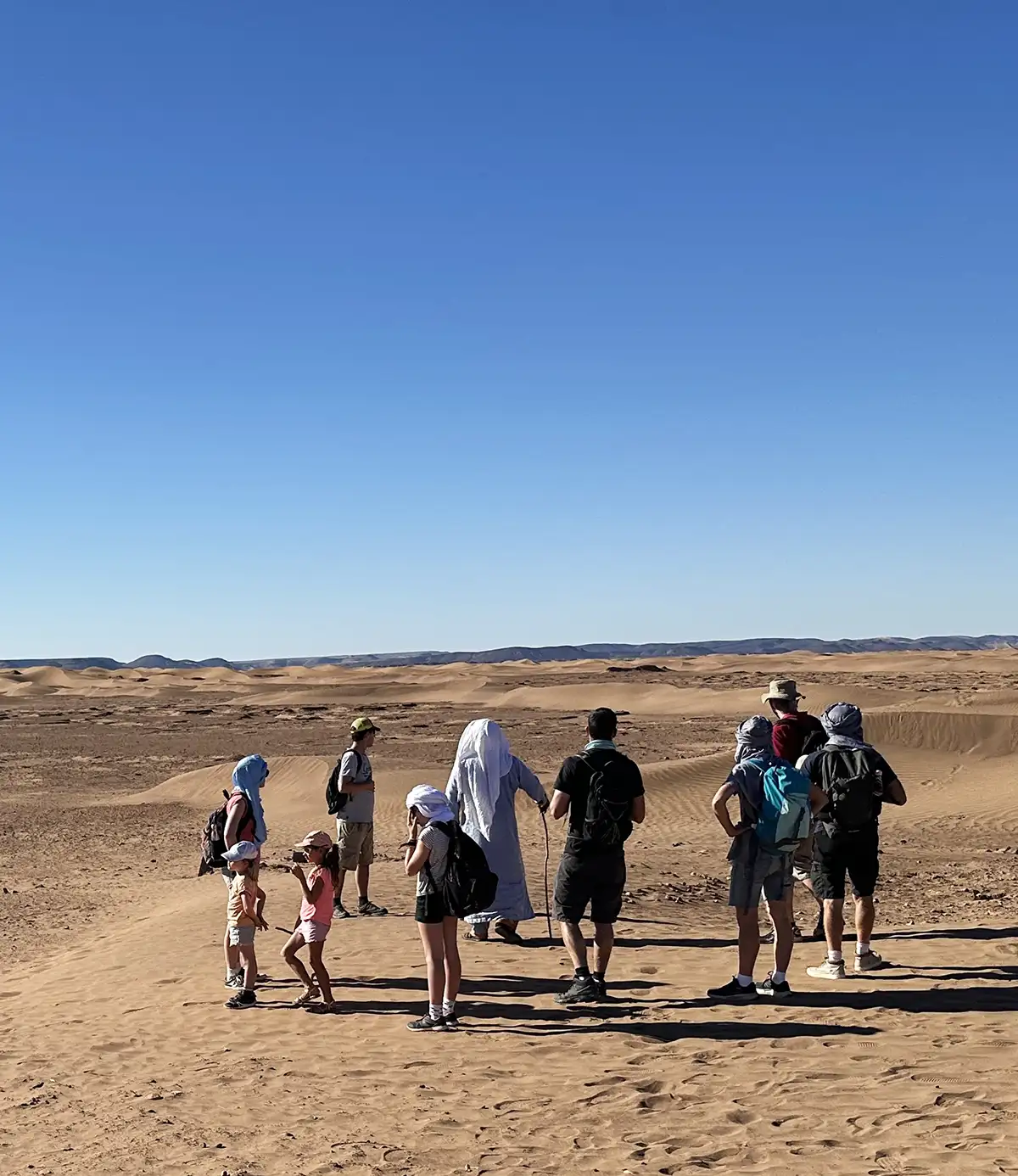 Travelers trekking through the Sahara desert with local nomad guides